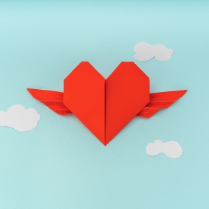 Red paper origami heart with wings and cloud on blue background